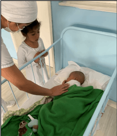   Genevieve conoce a su hermana pequeña (dormida) por primera vez.  